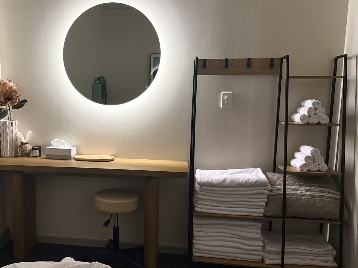 Backlit mirror, rolled towels and fresh linens in a Fern & Soul massage treatment room in Innaloo