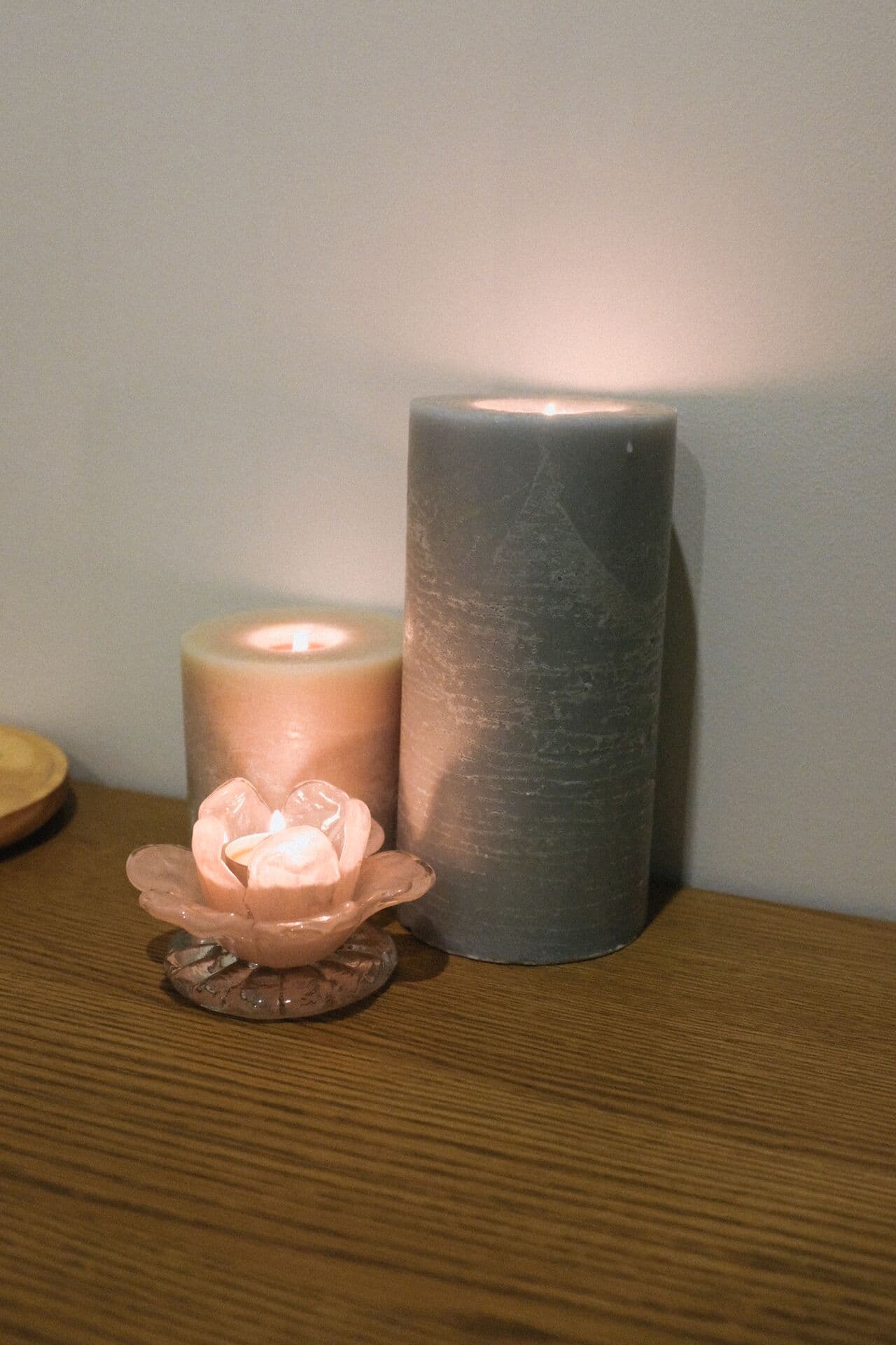 Lit pillar candles and a glass flower tealight holder on an oak console at Fern & Soul massage studio in Innaloo.