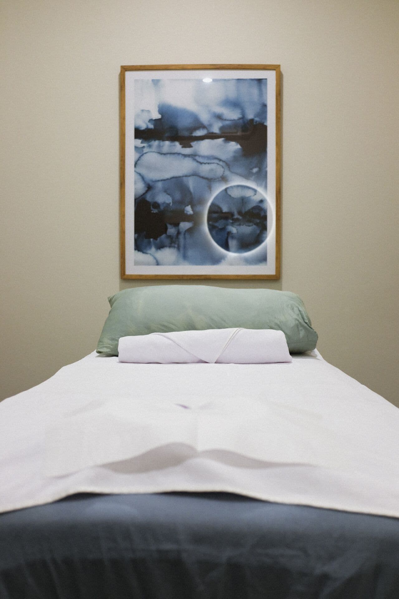 Massage table made up with a sage pillow and rolled towel beneath a framed watercolour print at Fern & Soul, Innaloo.