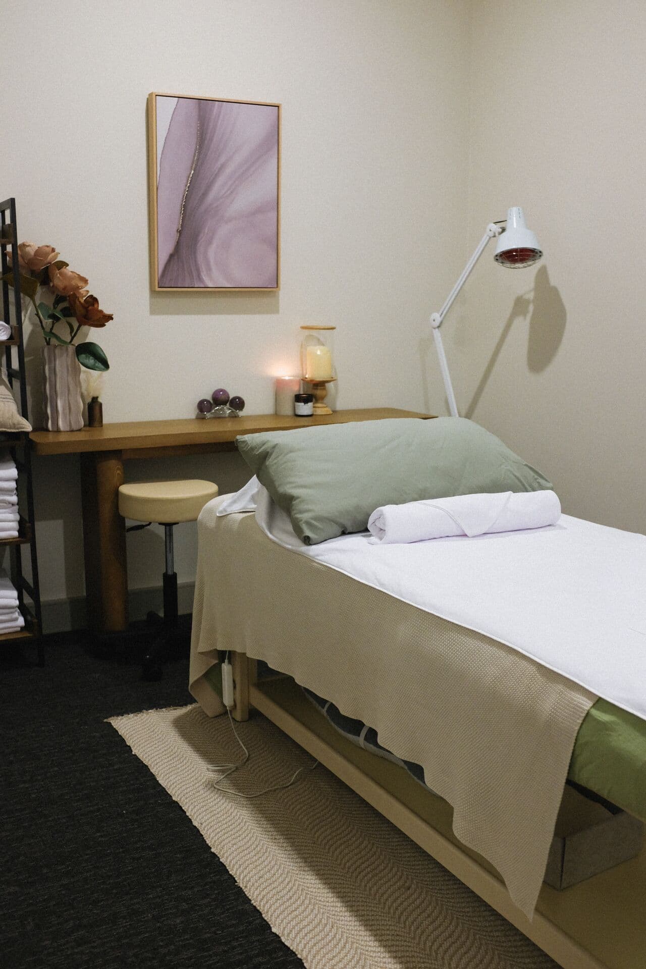 Side view of a remedial massage table at Fern & Soul in Innaloo, a sage pillow under a framed print and an infrared heat lamp.